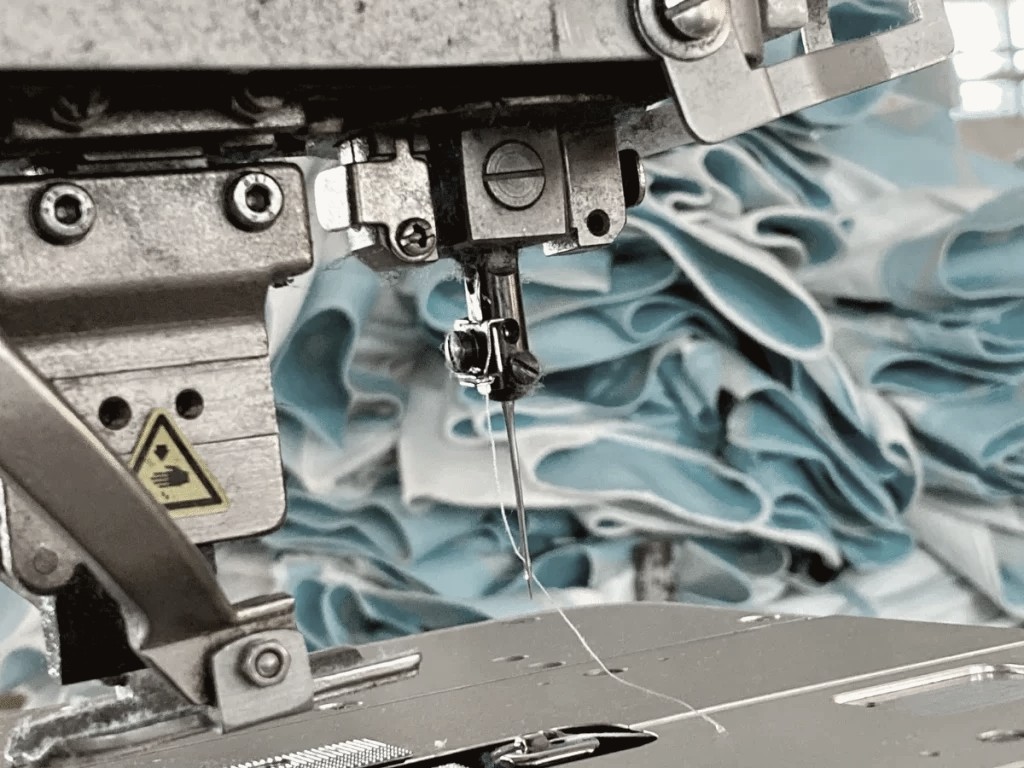 Industrial sewing machine needle stitching layered blue fabric for a small-batch production run at Thread Works Studios